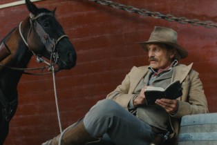 Man reading book next to horse in The Dead Dont Hurt