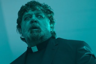 Russell Crowe in Priest outfit looking scared in blue light in The Exorcism